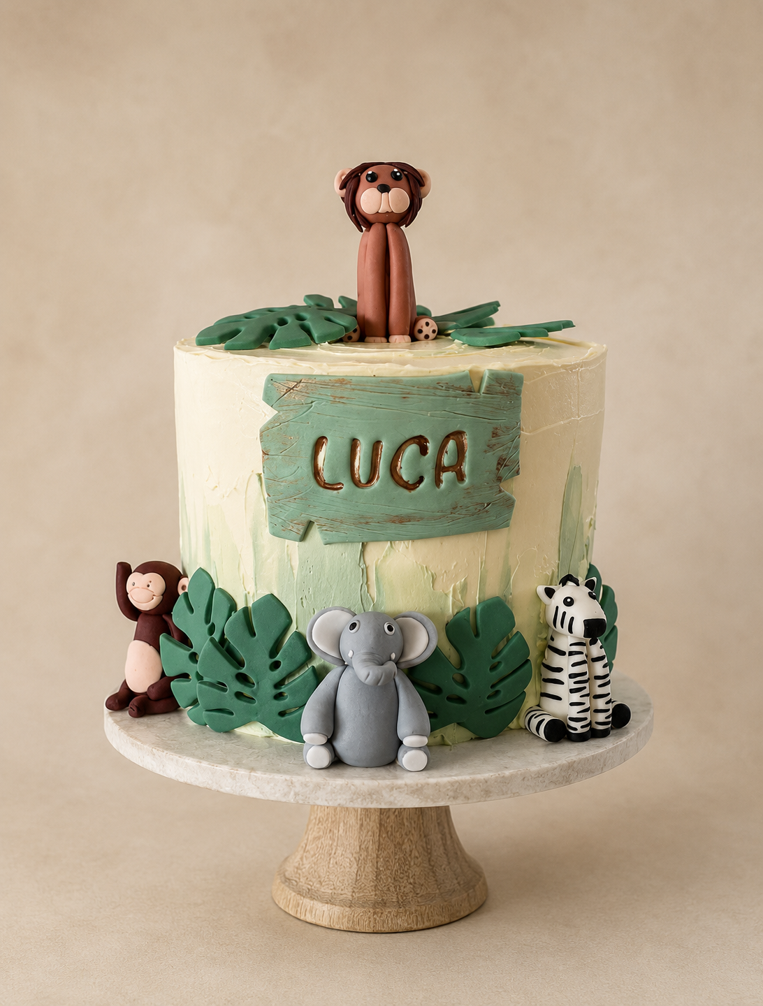 A custom safari-themed birthday cake with green leaf decorations and animal figurines, including a monkey, elephant, zebra, and another monkey, on a marble and wood cake stand. The side of the cake features a wooden sign with the name 'LUCA' in brown letters.