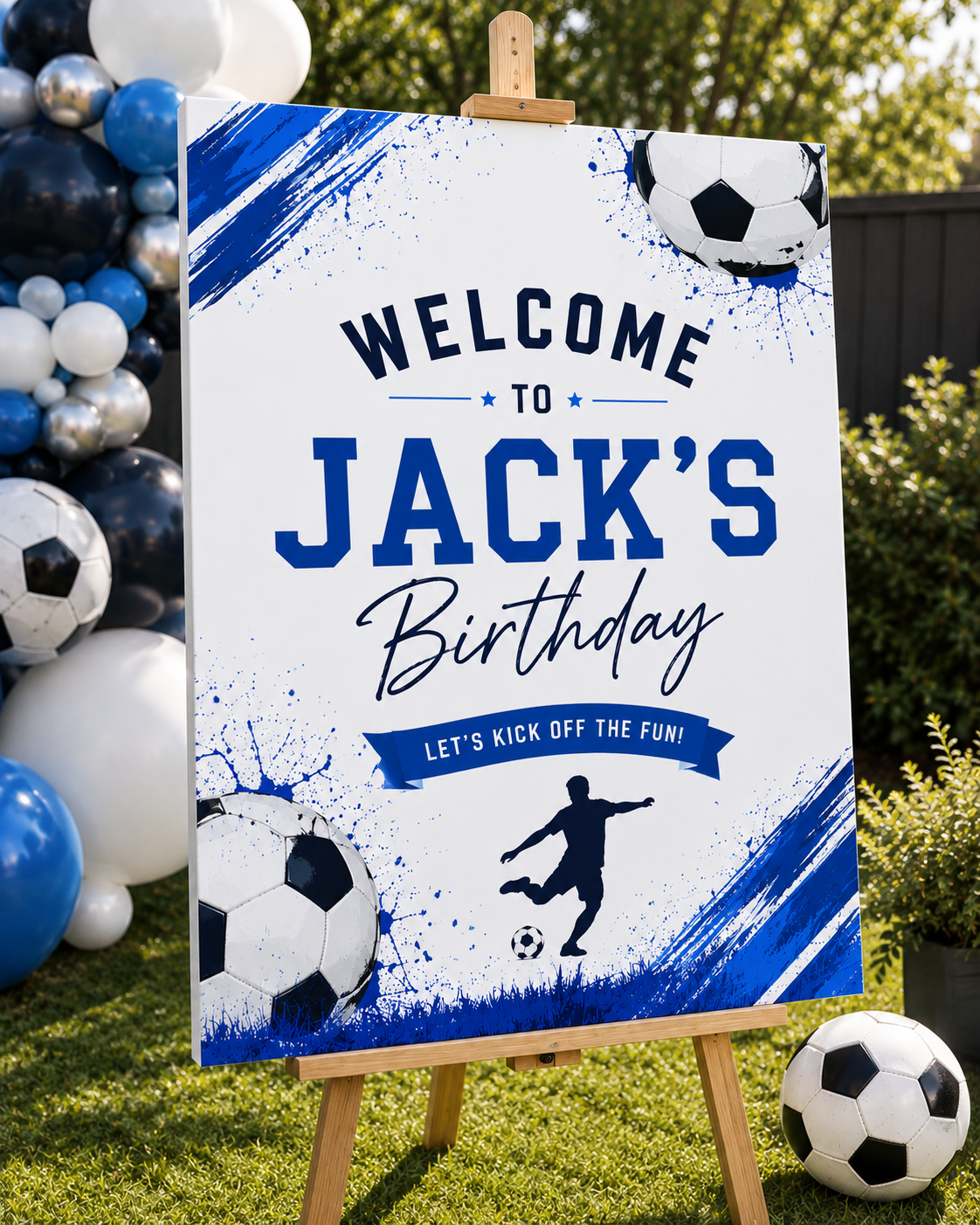 A customizable soccer-themed party sign reading 'WELCOME TO JACK'S Birthday' displayed on a wooden easel outdoors. The sign features a white background with blue paint splatters, soccer ball graphics, and a silhouette of a soccer player.