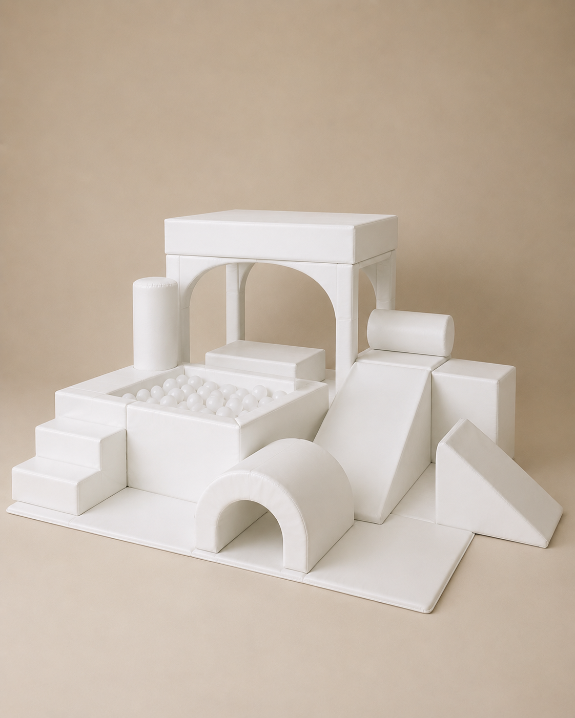 White geometric children's play structure with blocks, arches, stairs, and a ball pit, photographed on a warm beige studio background.