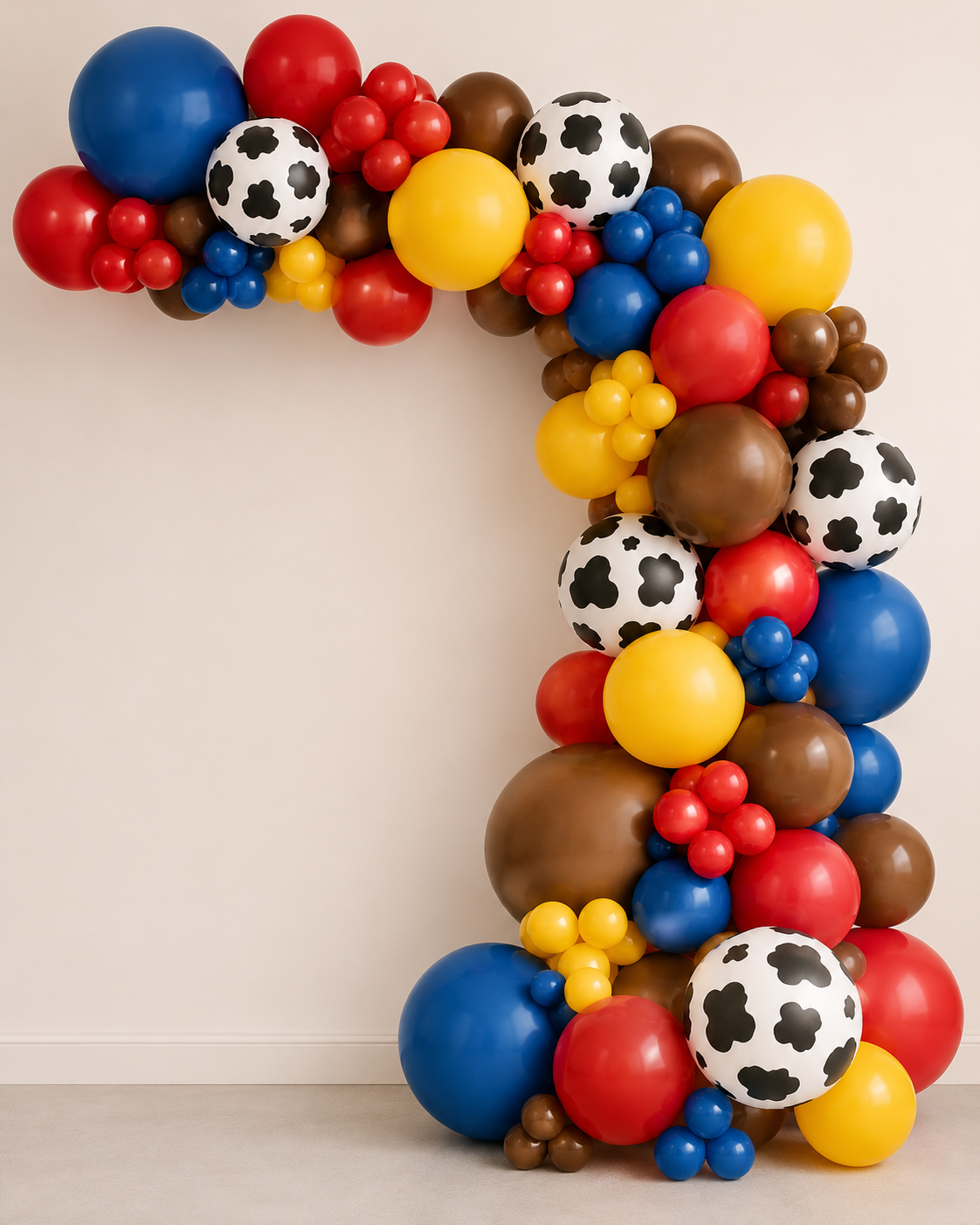 A large balloon garland arch decorated with red, blue, yellow, and brown balloons, including soccer-ball patterned balloons, arranged in a U-shape against a plain beige wall.